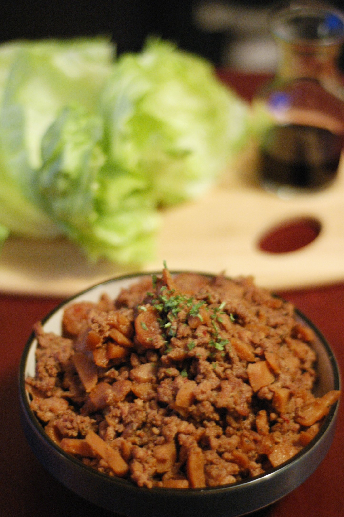 Black bowl with pork mixture with head of lettuce on cutting board in background