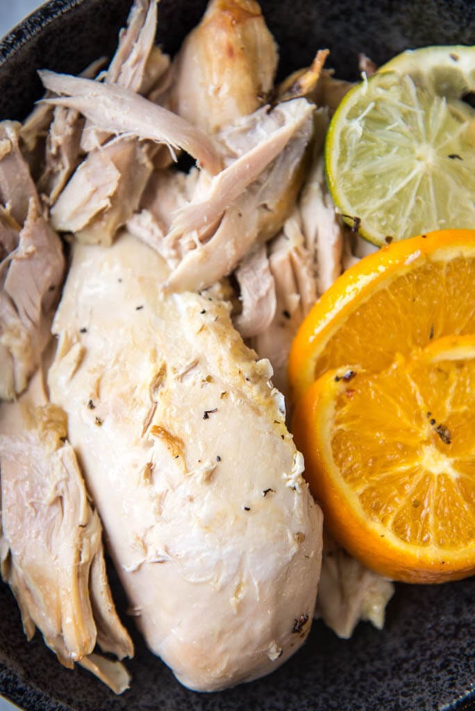 Shredded slow cooker whole chicken with lemon and lime slices on the side, placed on a black plate.