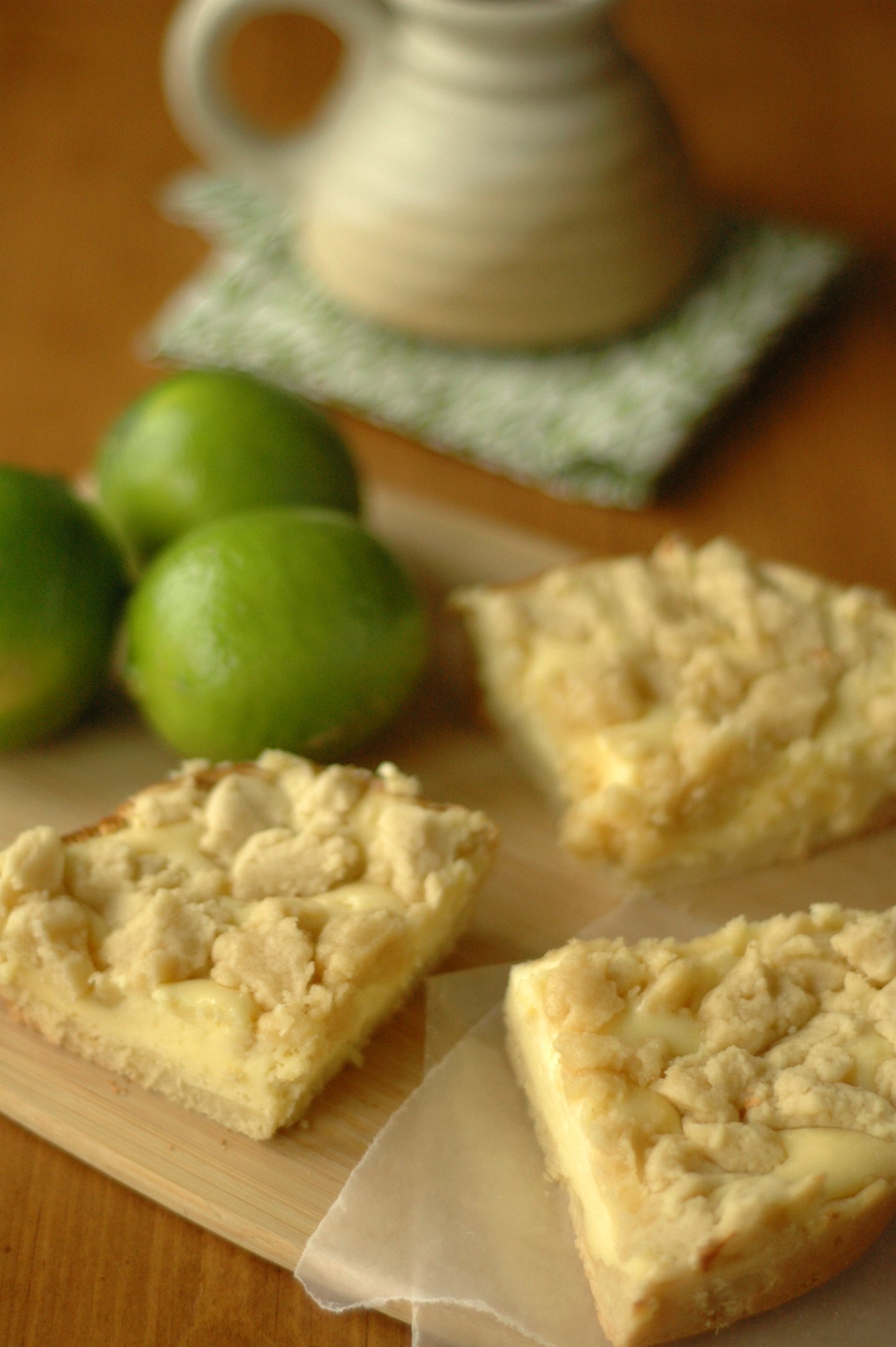 Three cheesecake cookie bars on cutting board with limes