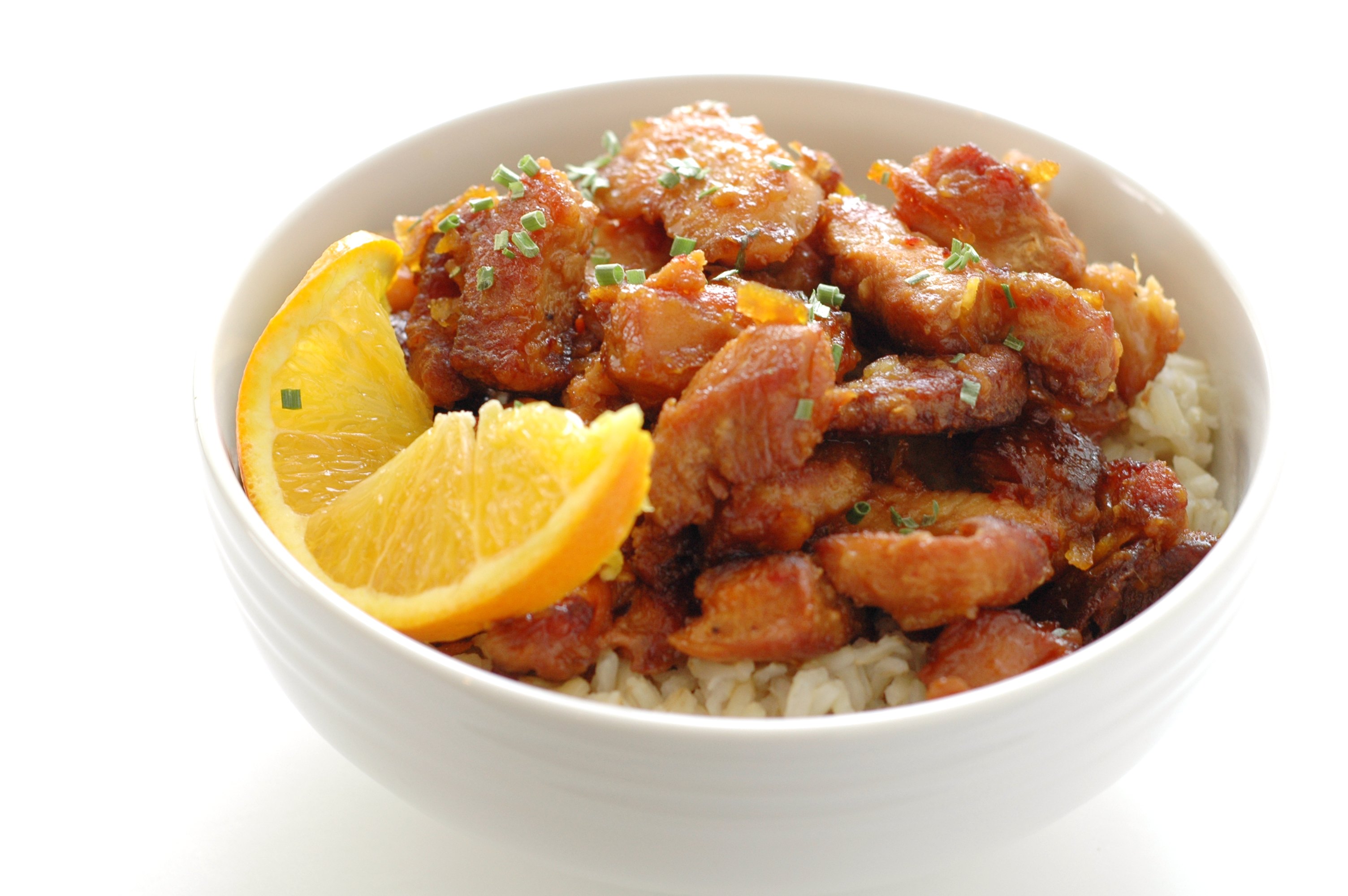 side view of white bowl with orange chicken on bed of rice with slice of orange
