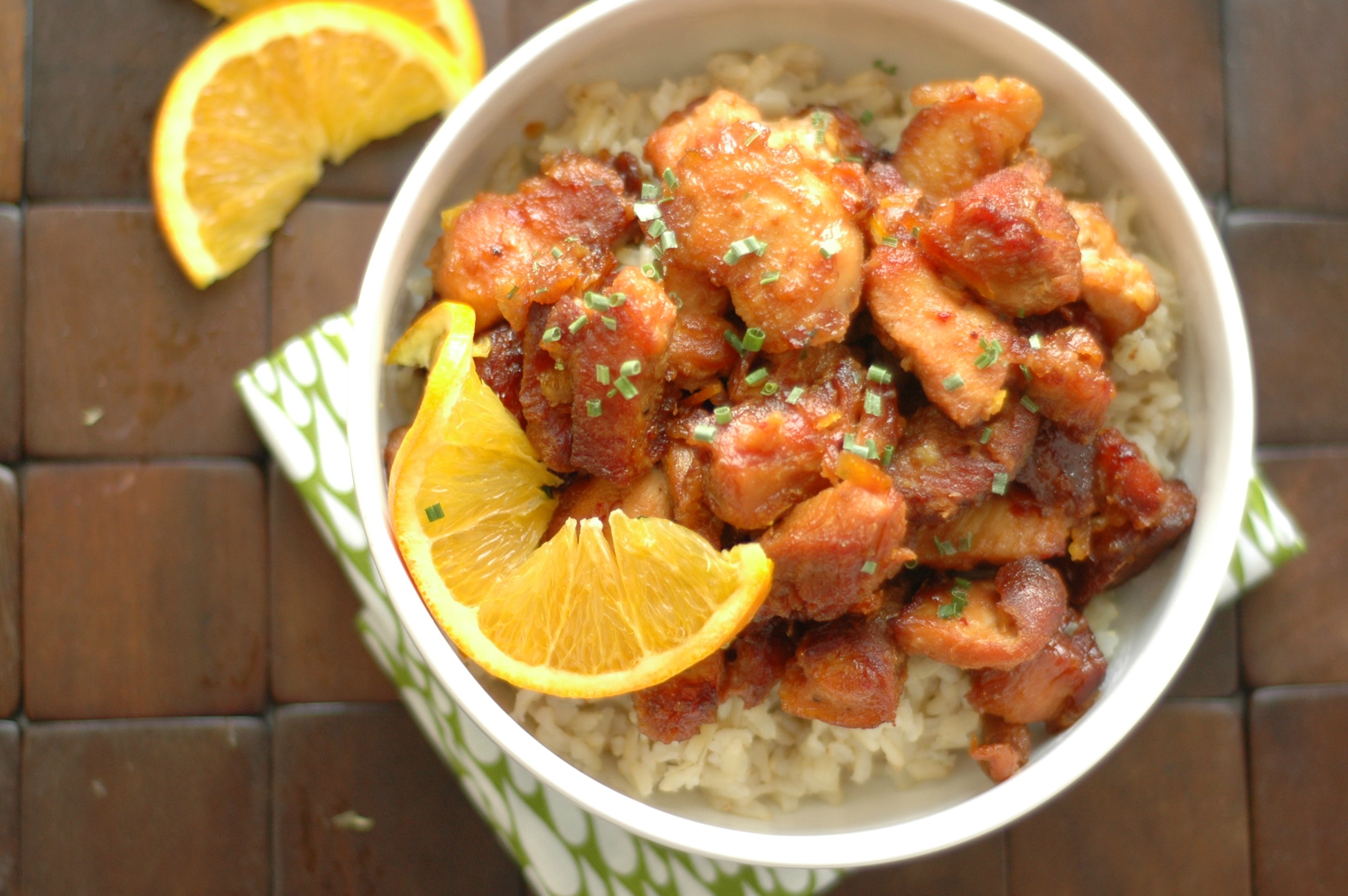 top view of orange chicken on bed of rice with slice of orange