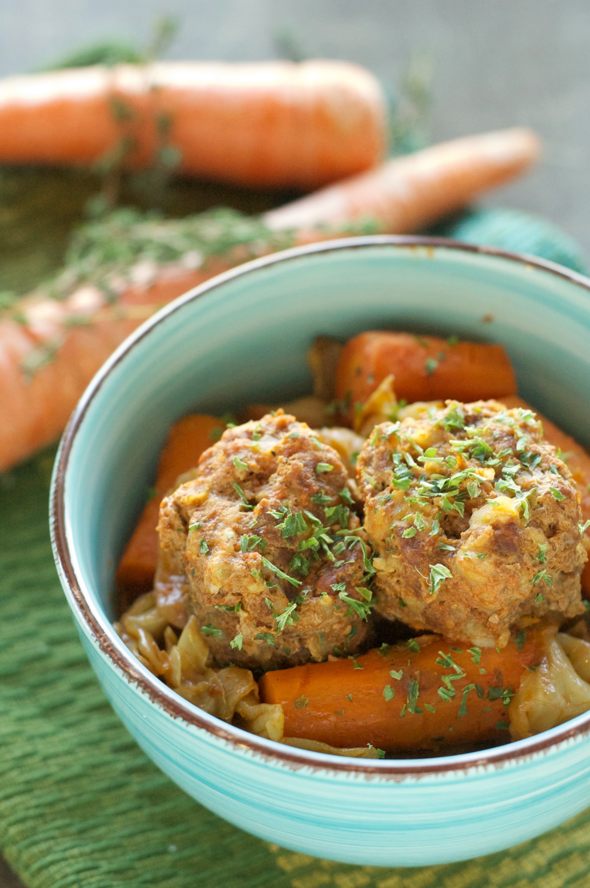 green bowl with two meatballs, carrots and cabbage on green placemat with two carrots in background