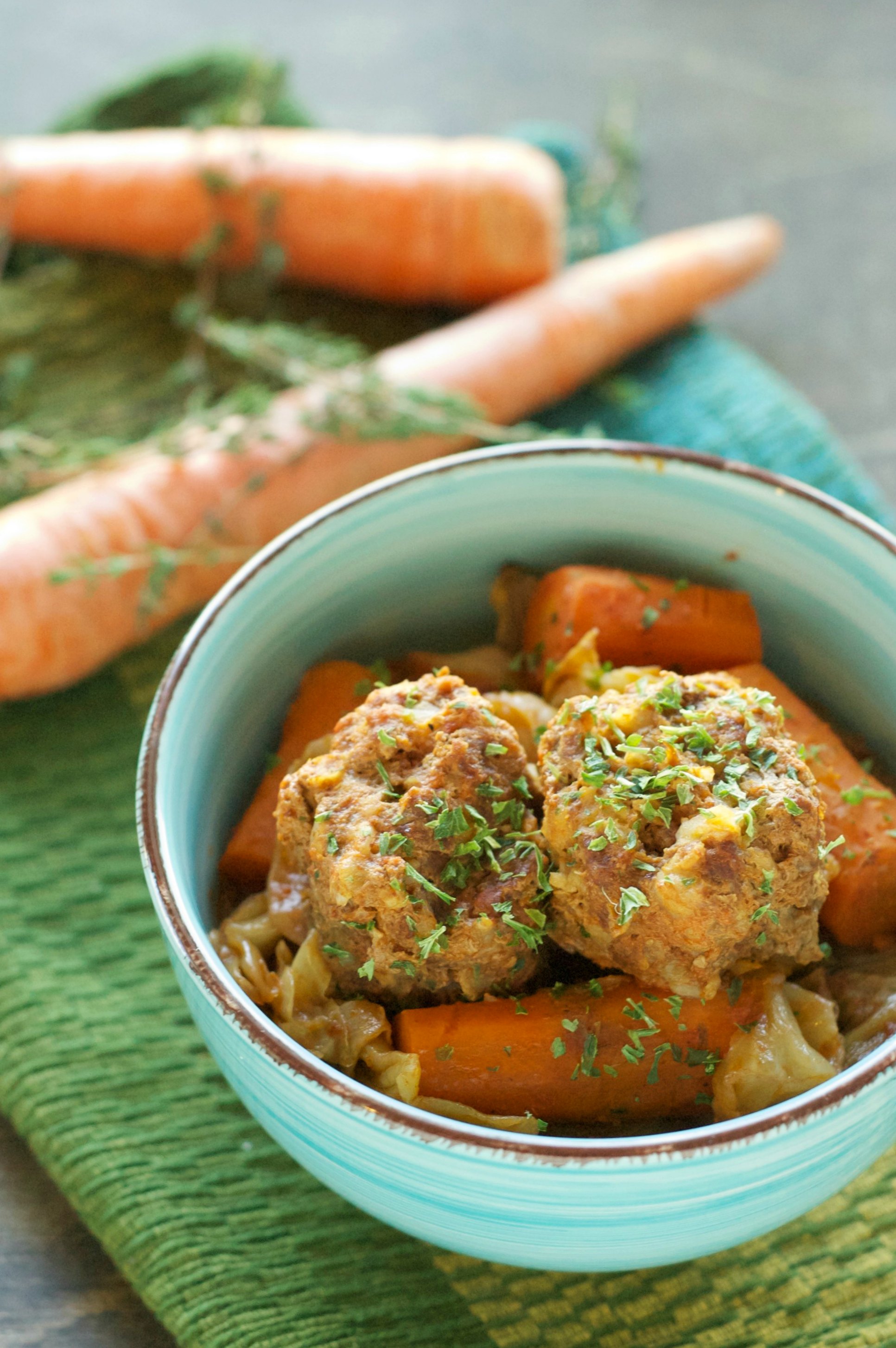 green bowl with meatballs and carrots with two carrots in background