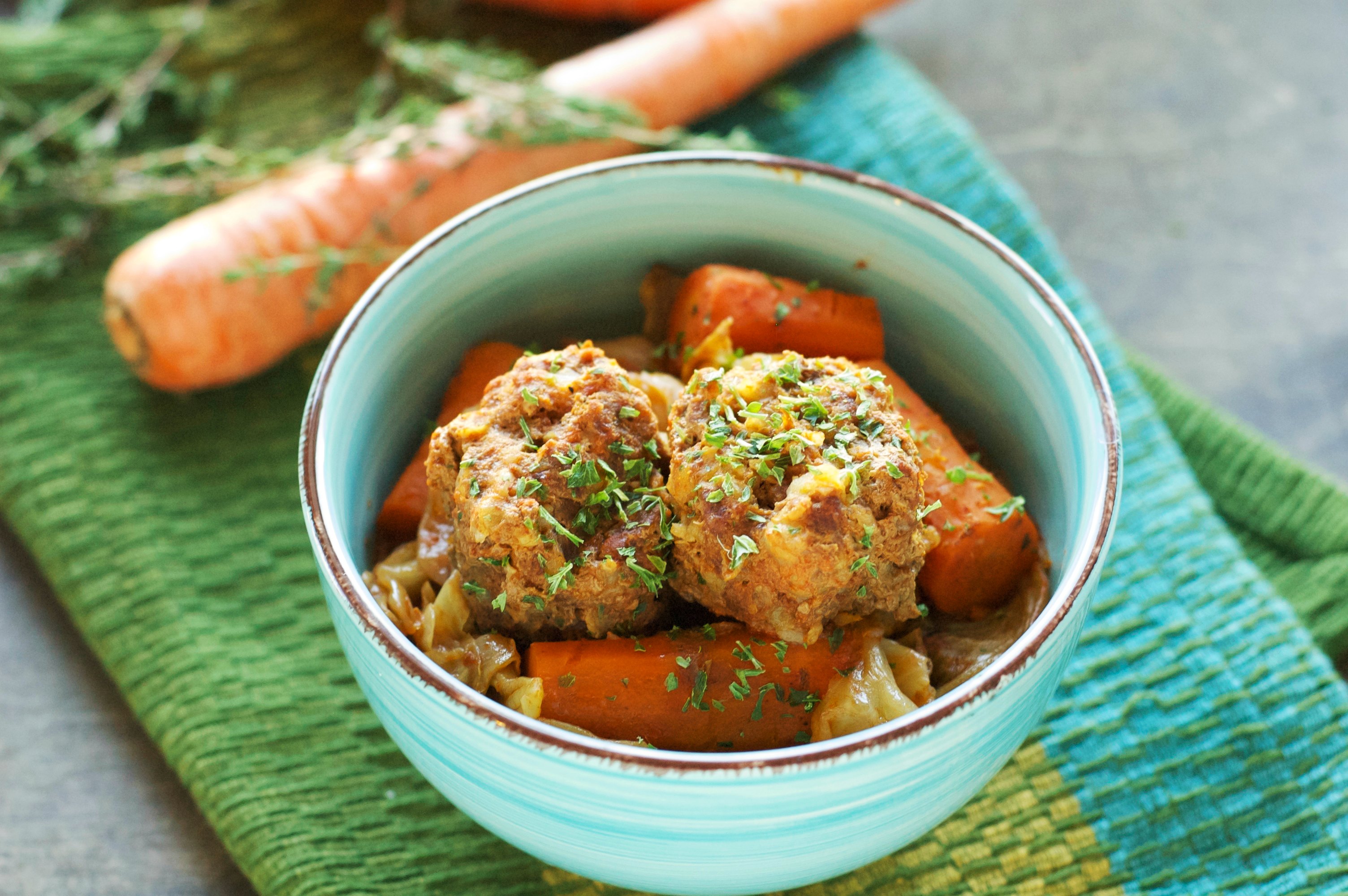 green bowl with meatballs and carrots with one carrot in background