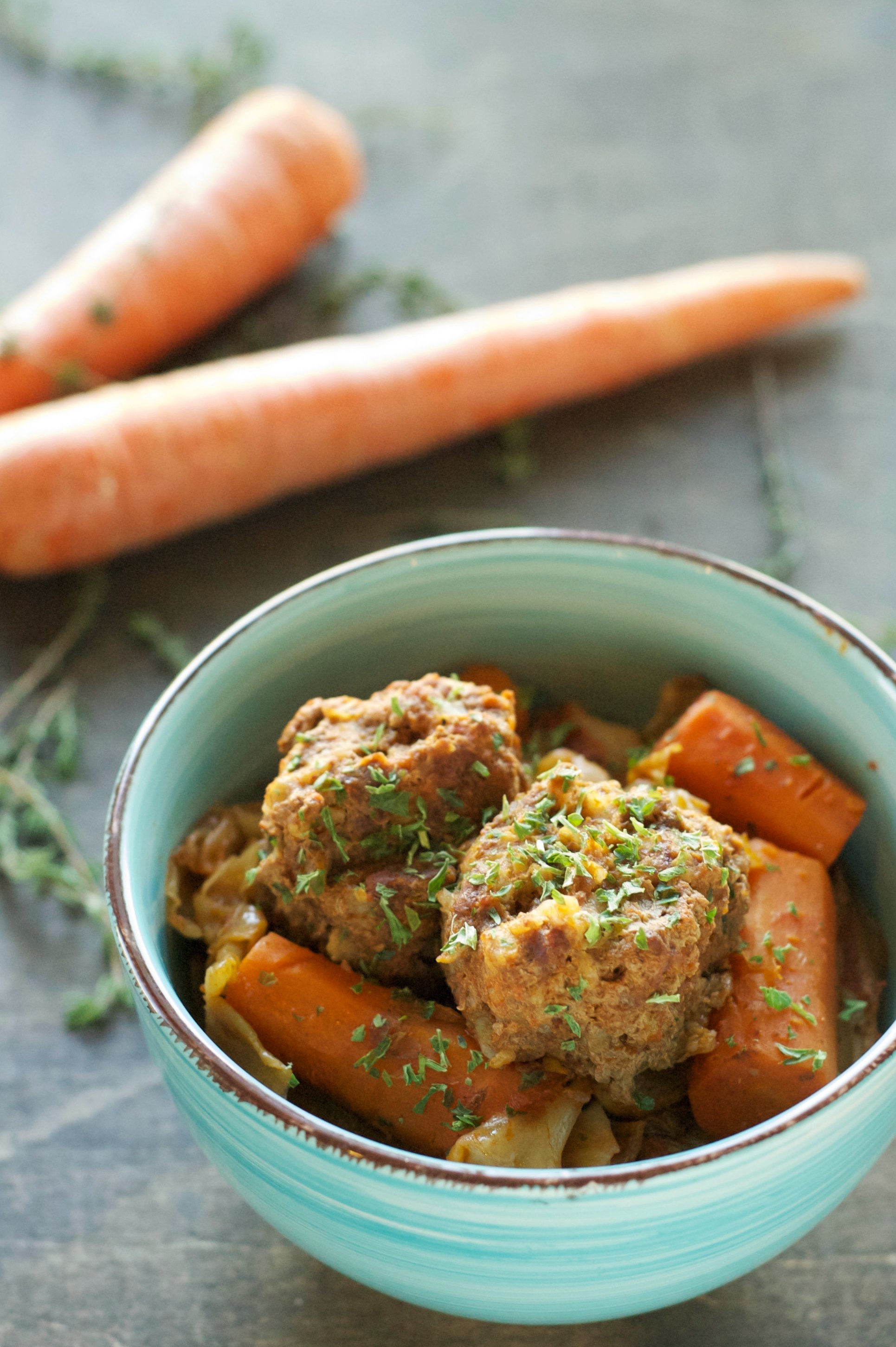 green bowl with meatballs and carrots with carrots in background