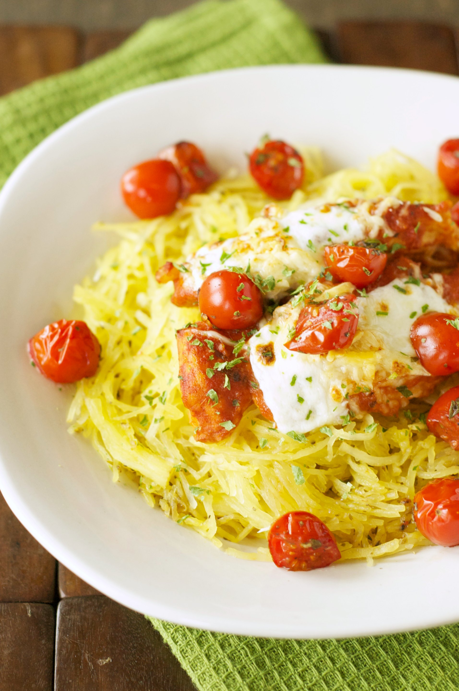 roasted tomatoes and chicken on bed of spaghetti squash in white bowl on green towel
