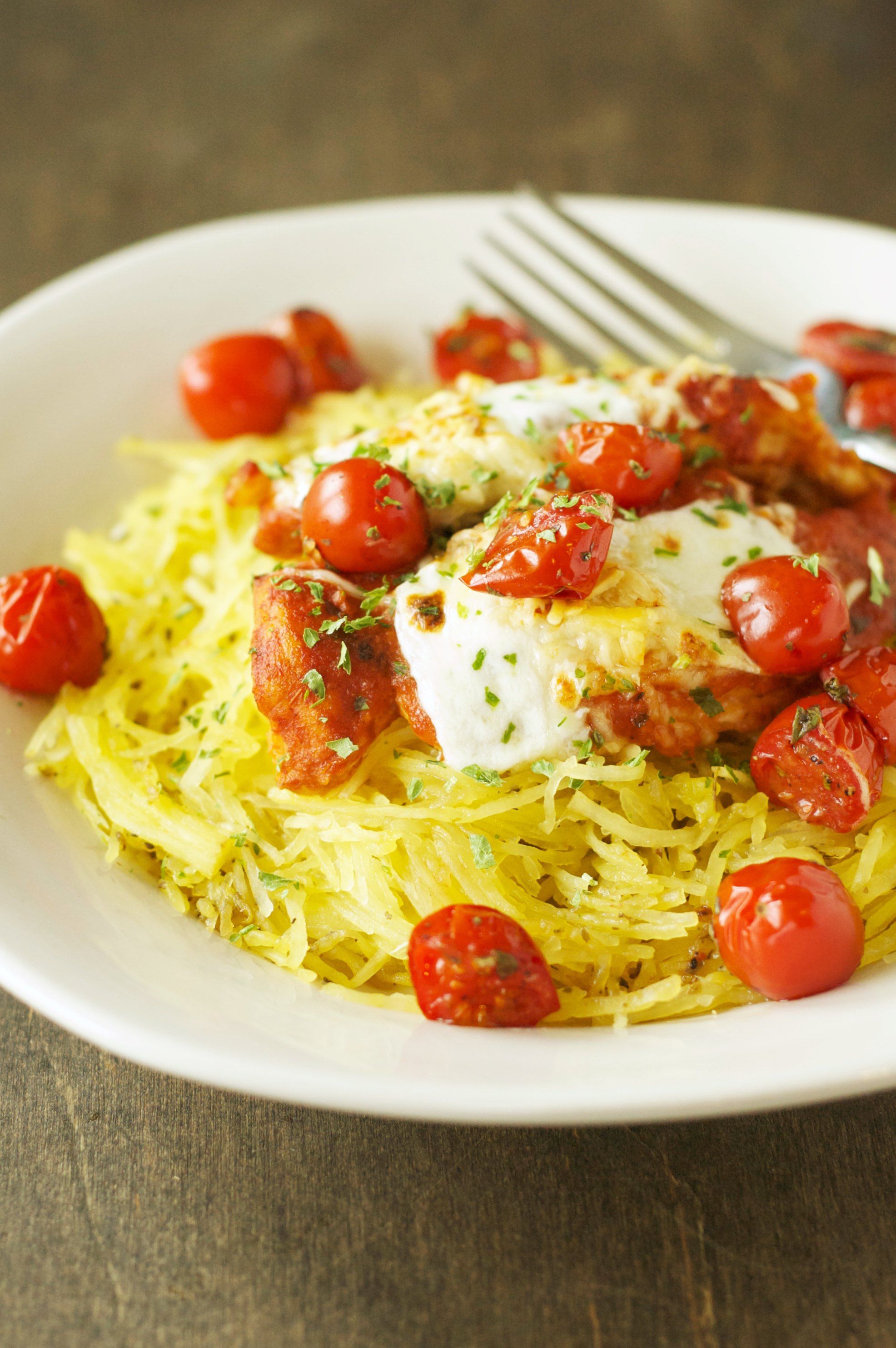 chicken and tomatoes on bed of spaghetti squash in white bowl