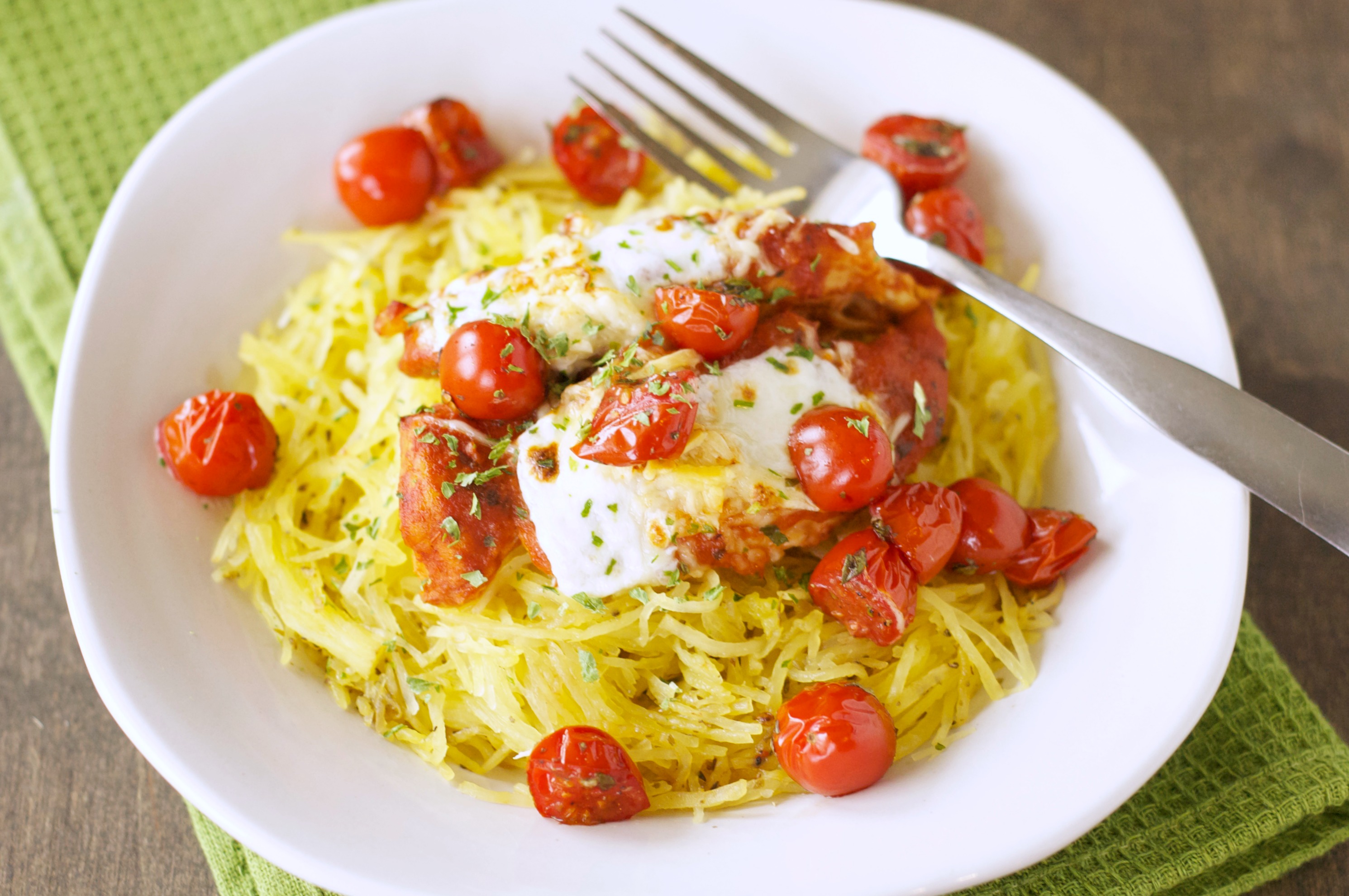 front view of white bowl with chicken and roasted tomatoes on bed of spaghetti squash on green towel 
