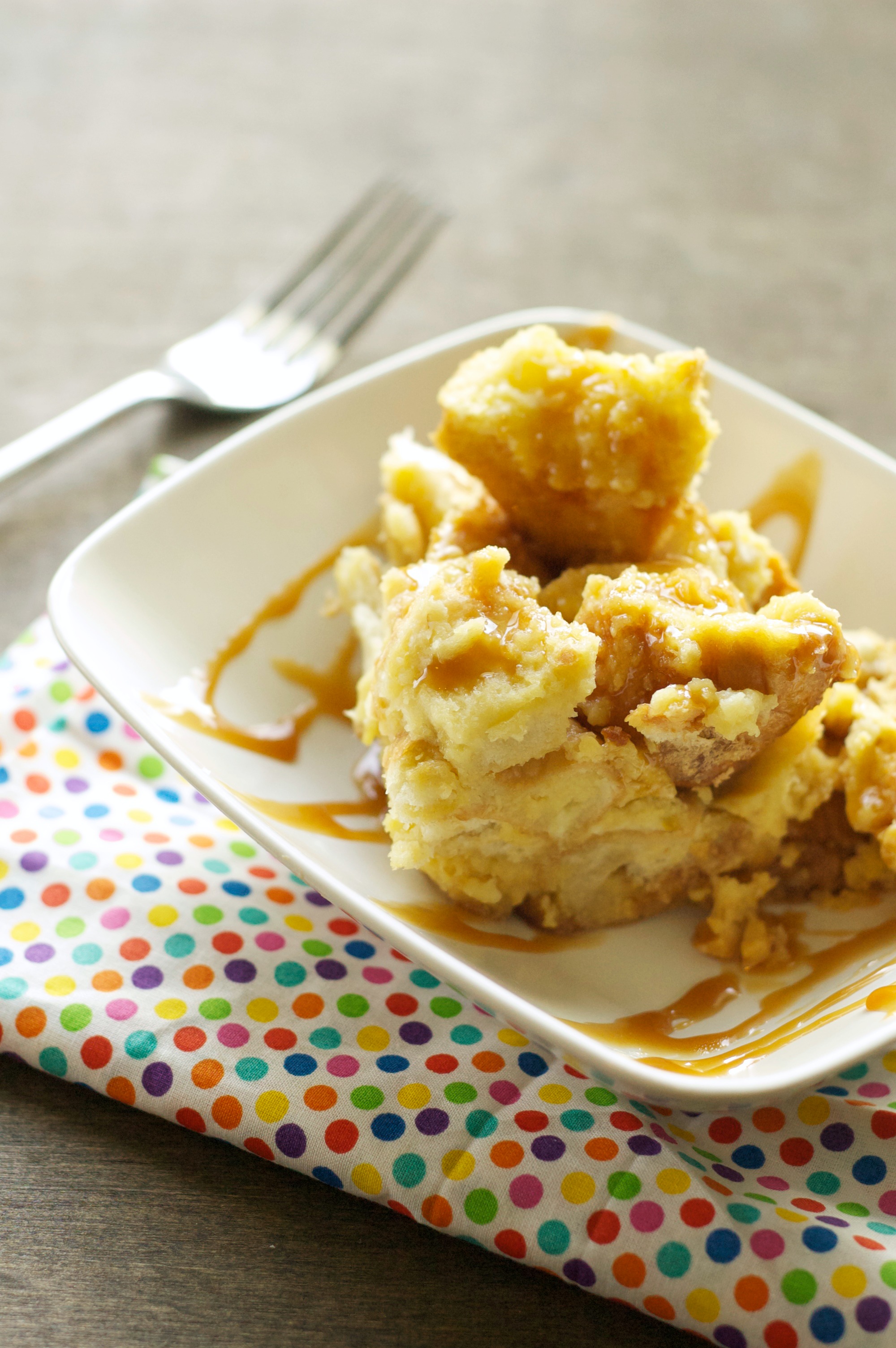 Slow Cooker Bread Pudding with Salted Caramel Sauce in white bowl on polka dot napkin with fork in background