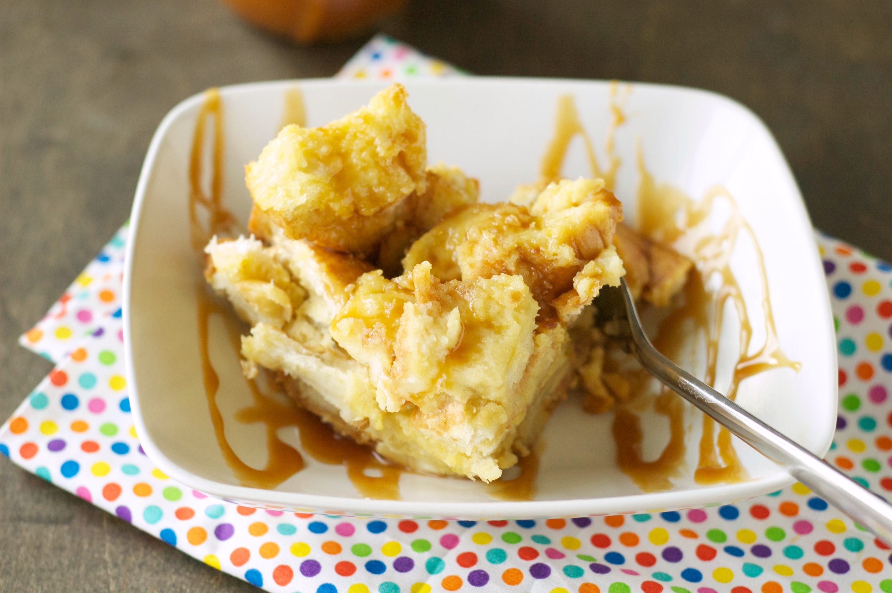 Top side view of Slow Cooker Bread Pudding with Salted Caramel Sauce in white bowl on polka dot napkin