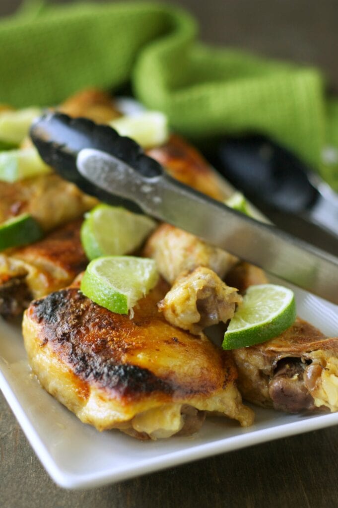 Slow Cooker Coconut Lime Chicken on white plate with tongs and lime slices
