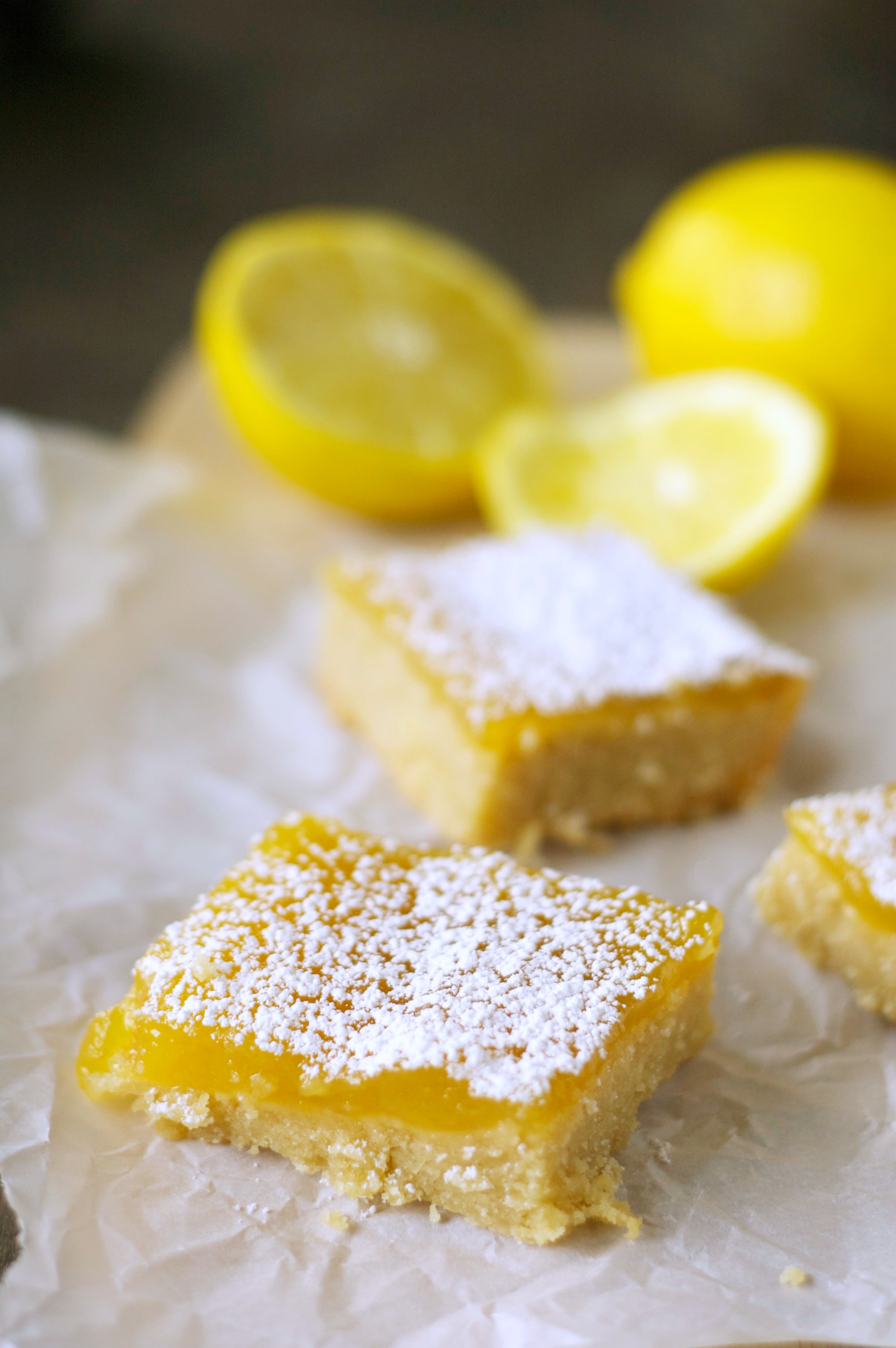 Three pieces of Lemon Cookie Bars with lemons in the background