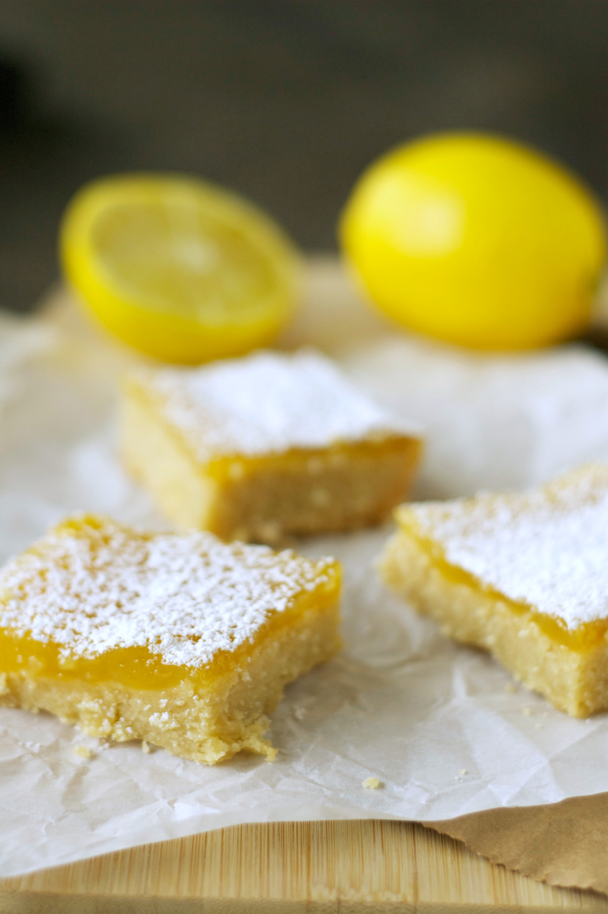 Three pieces of Lemon Cookie Bars with lemons in the background