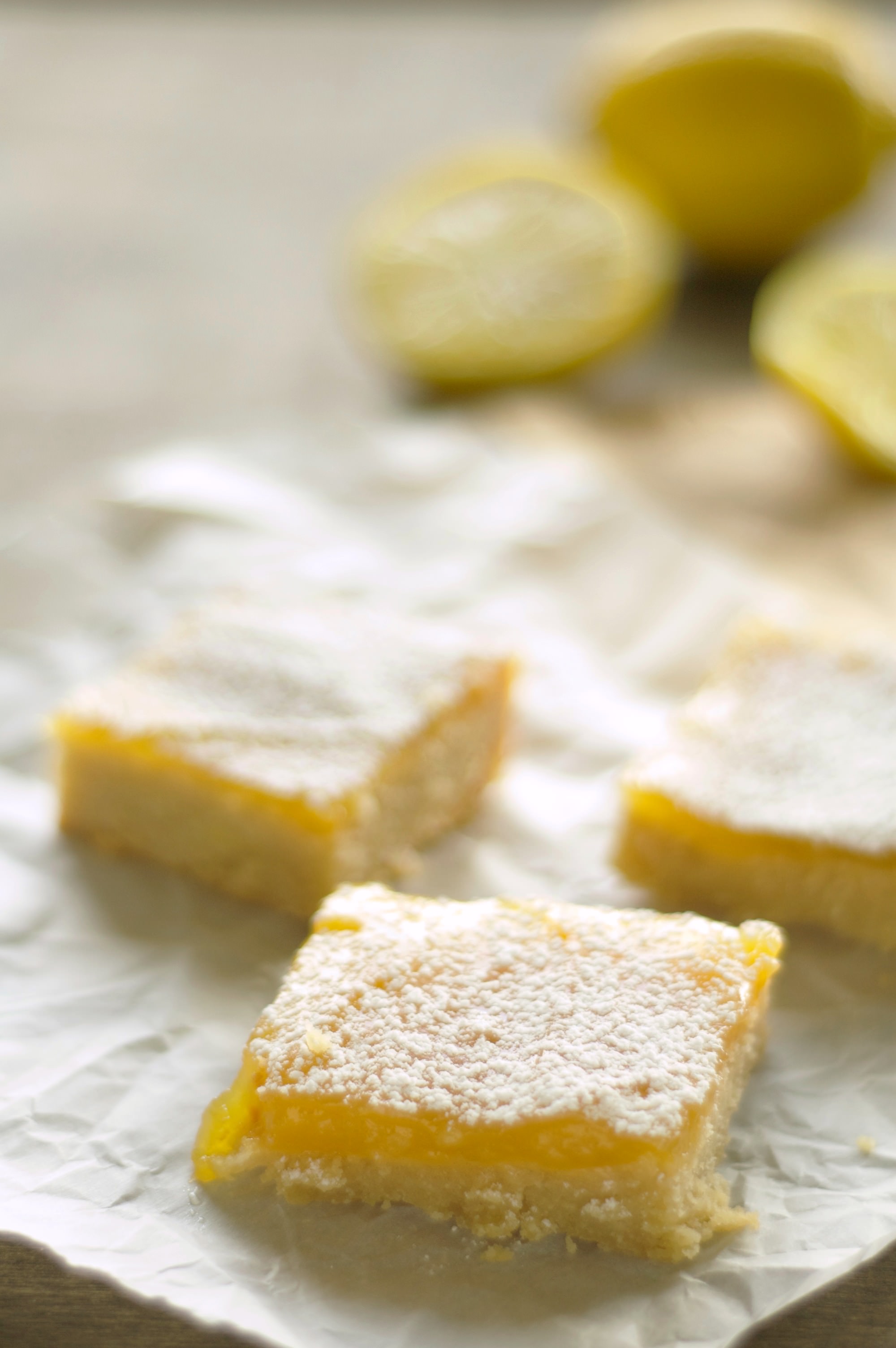 Three pieces of Lemon Cookie Bars with lemons in the background