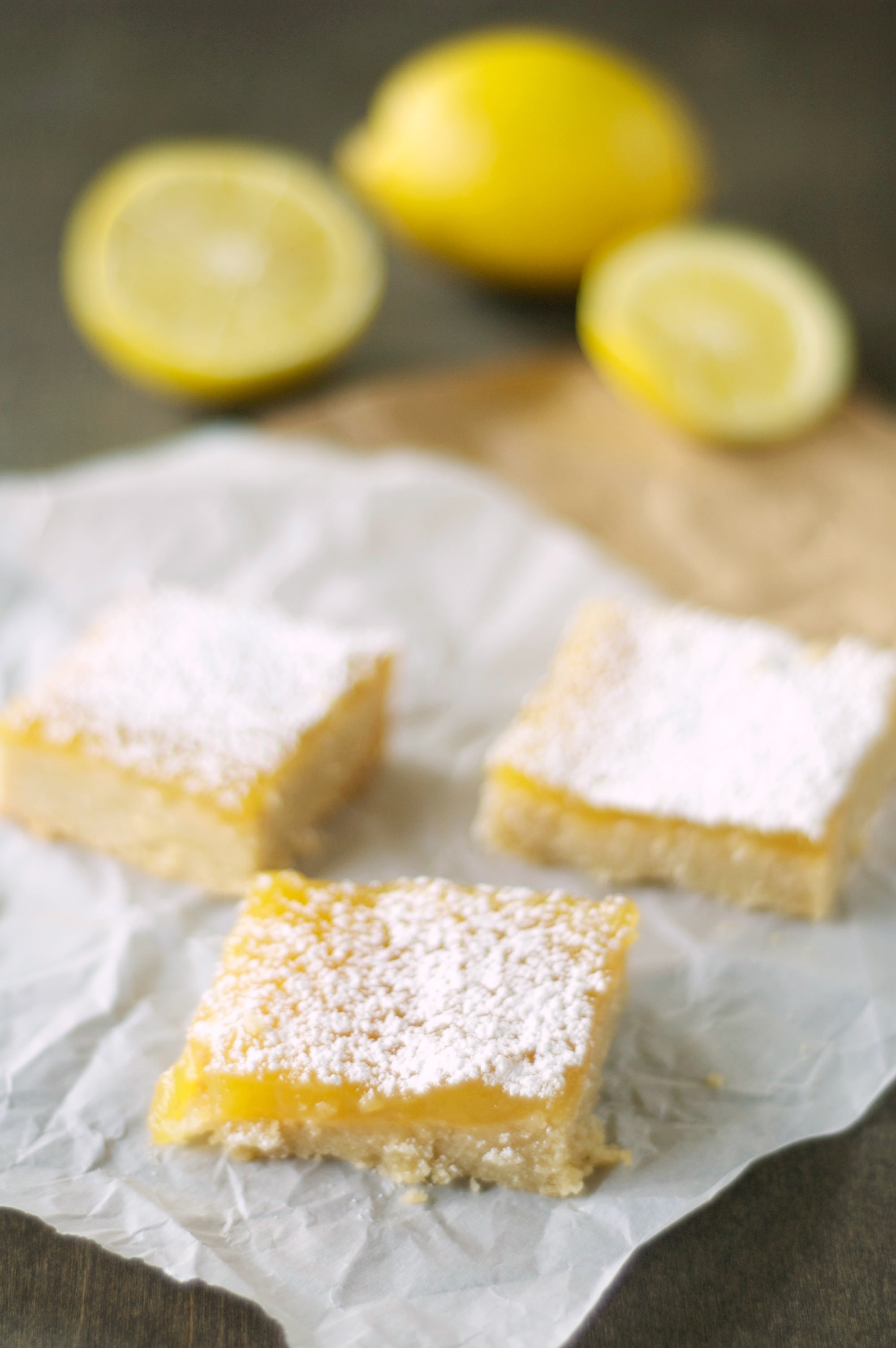 Three pieces of Lemon Cookie Bars with lemons in the background