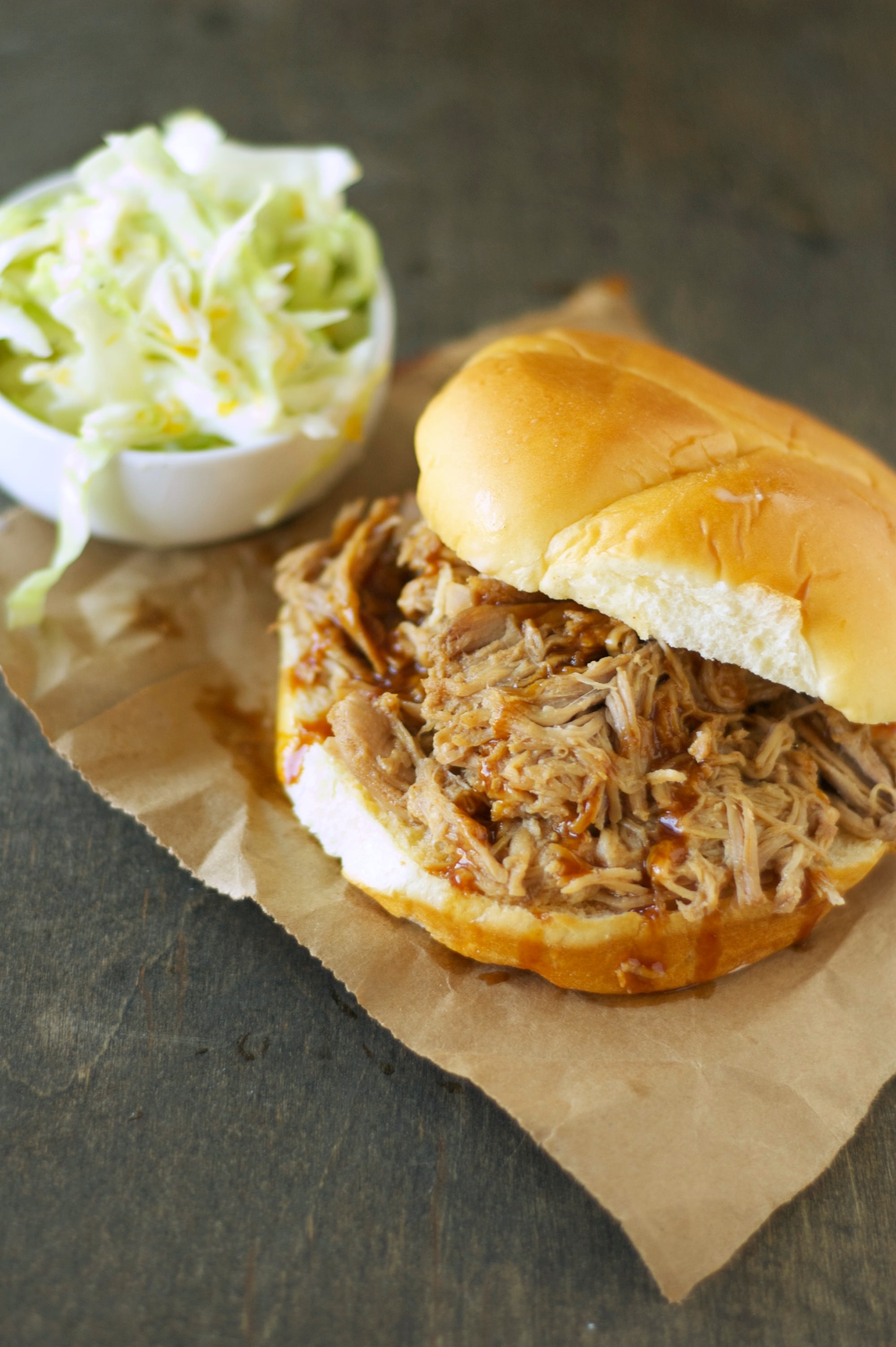 Slow Cooker Pulled Pork on bun with bowl of slaw