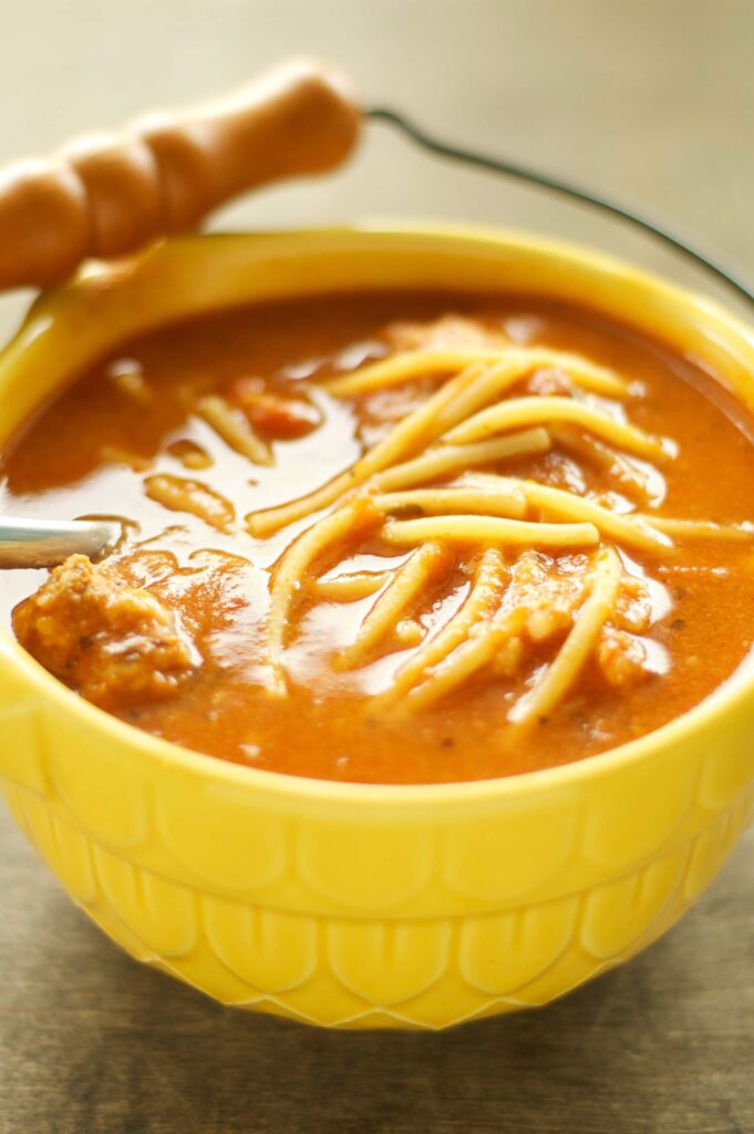 Slow Cooker Spaghetti and Meatball Soup in yellow bowl with wooden handle