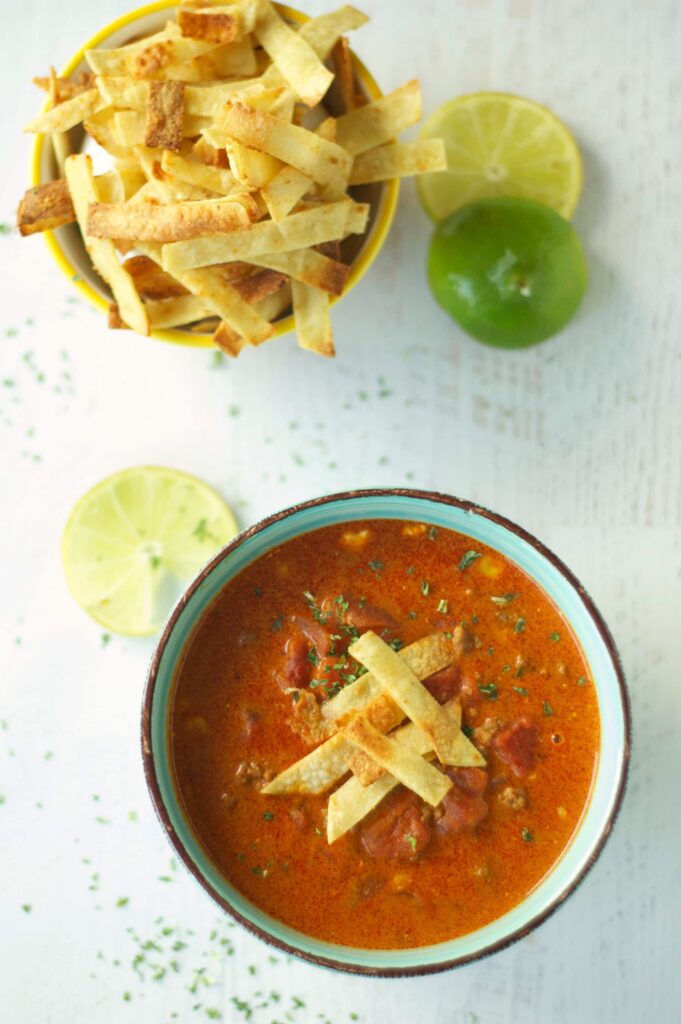 Slow Cooker Beef Enchilada Soup in green bowl with tortilla strips and lime slices 