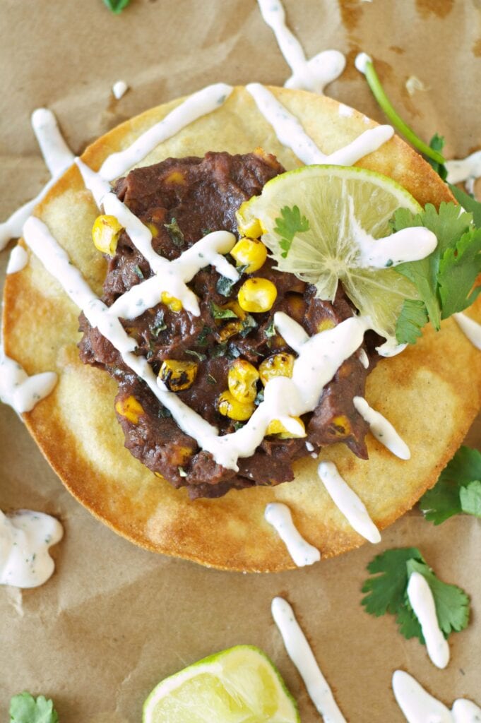 Slow Cooker Black Bean, Corn and Basil Tostada on wax paper with sour cream drizzle