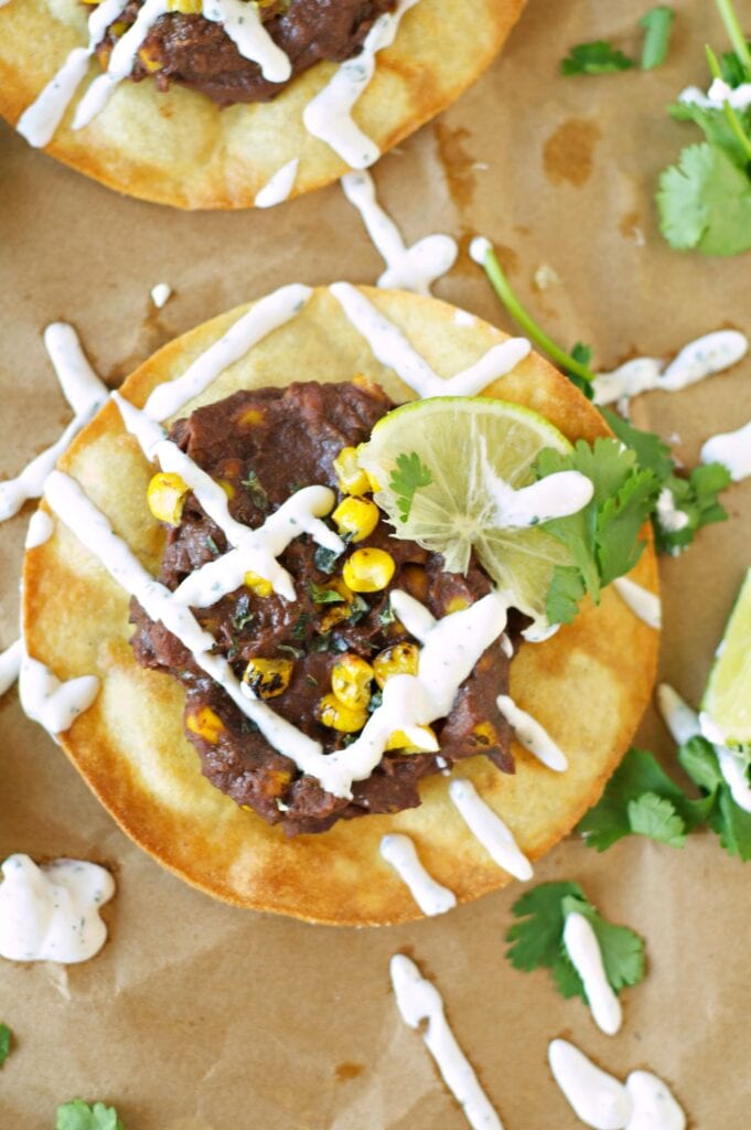 Slow Cooker Black Bean, Corn and Basil Tostadas on wax paper with sour cream drizzle