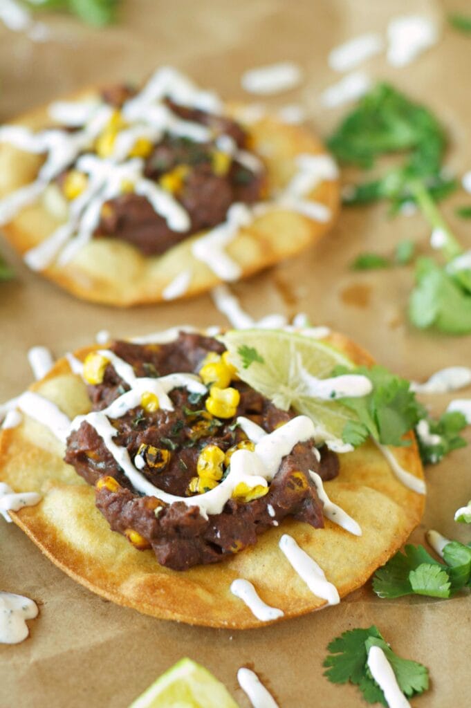 Two Slow Cooker Black Bean, Corn and Basil Tostadas on wax paper with sour cream drizzle 