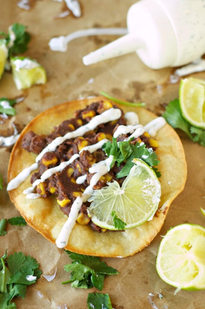 Slow Cooker Black Bean, Corn and Basil Tostadas on wax paper with sour cream drizzle
