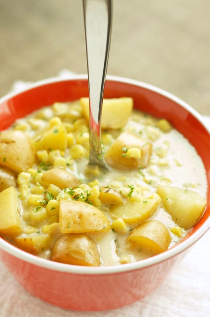 Slow Cooker Corn and Potato Chowder in red bowl with spoon