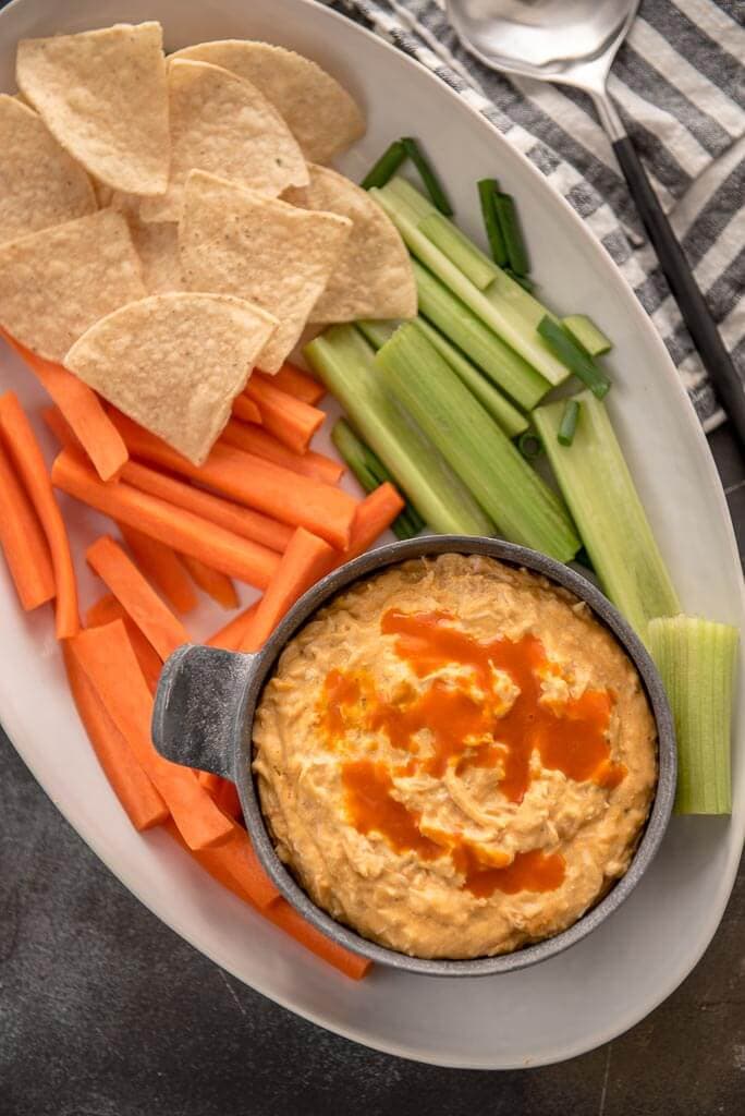 Cheesy Slow Cooker Buffalo Chicken Dip served in metal bowl on white platter with veggies and chips
