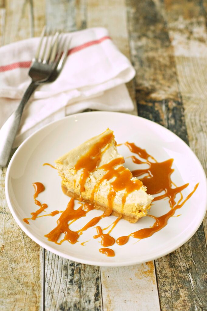Slice of Slow Cooker Browned Butter Pumpkin Cheesecake on white plate with fork and napkin