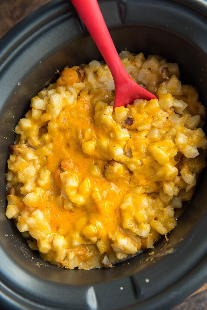Overhead view of Slow Cooker Cheesy Potatoes in an oval slow cooker with a red spoon