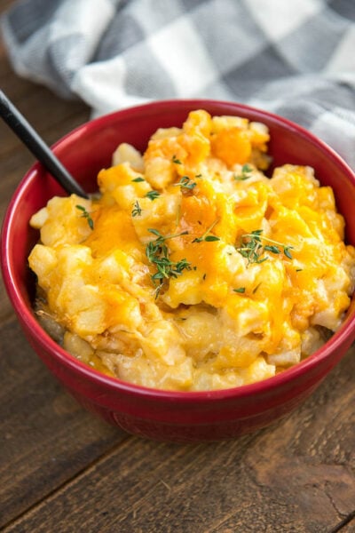 Slow Cooker Cheesy Potatoes in a red bowl with a white and gray checkered napkin
