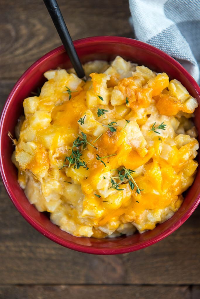 Slow Cooker Cheesy Potatoes in a red bowl, with a black utensil and a gray and white checkered napkin