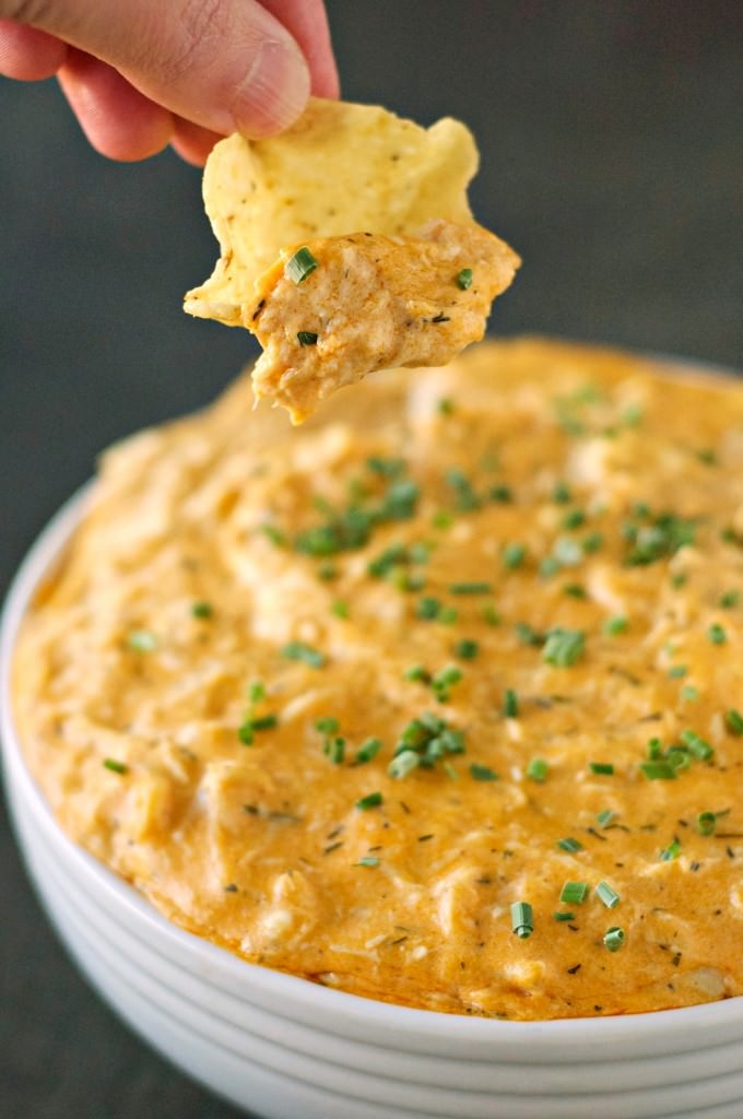 white bowl containing buffalo chicken dip with hand holding chip and dip