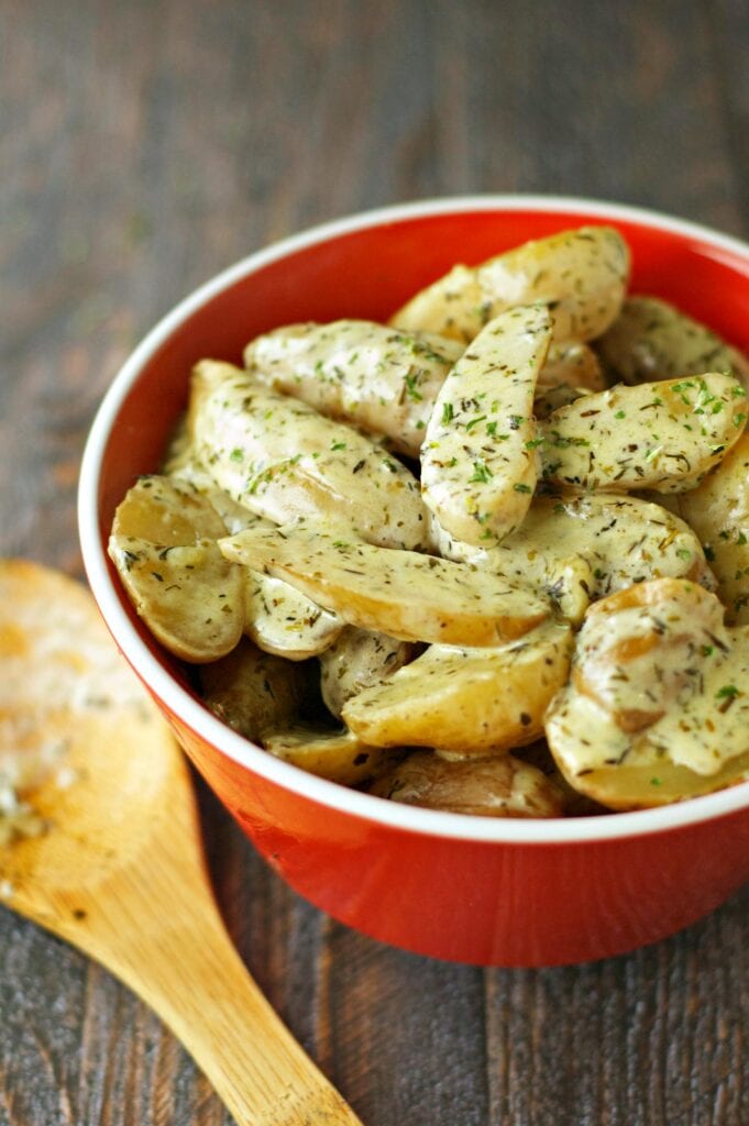 Slow Cooker Creamy Cheesy Fingerling Potatoes in red bowl on white napkin with wooden spoon