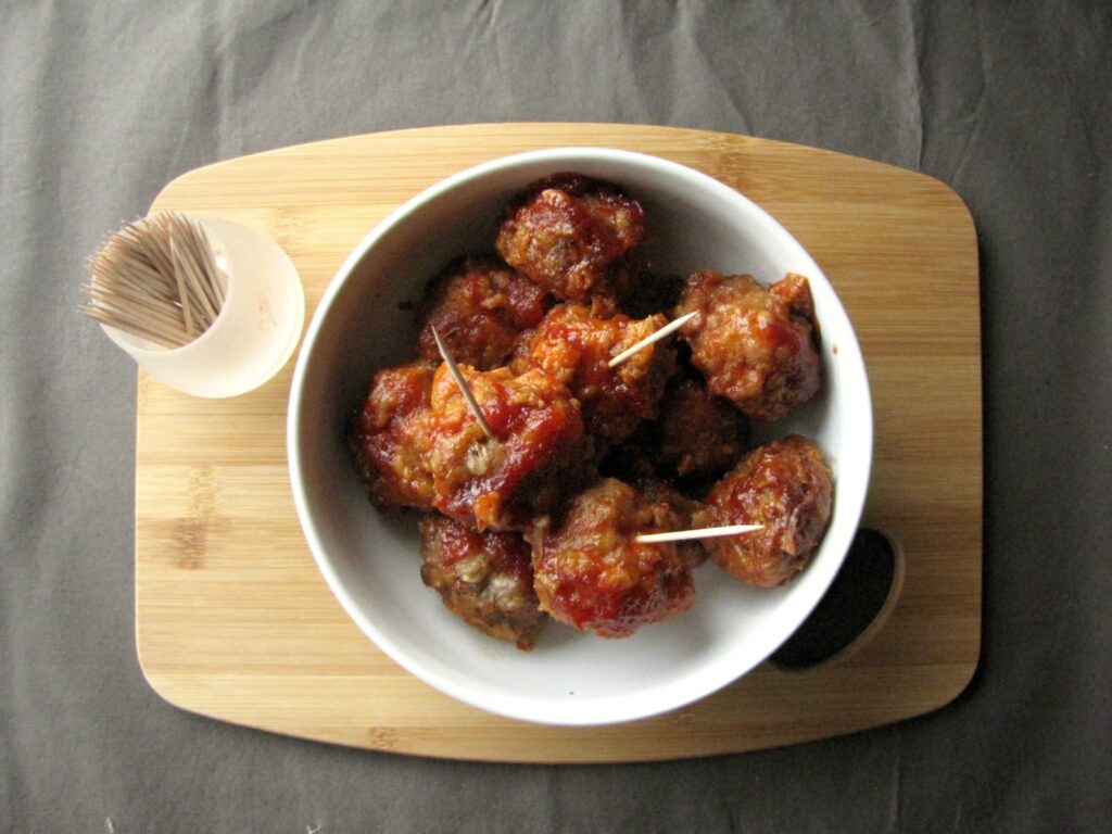 meatballs with toothpicks in white bowl on wooden cutting board