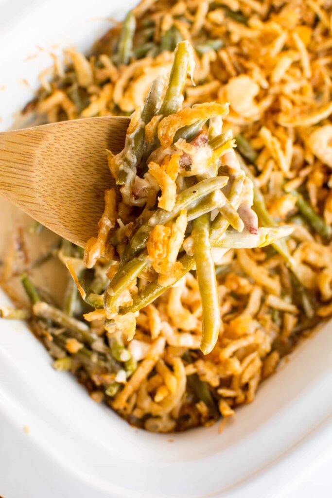  Overhead view of Slow Cooker Fresh Green Bean Casserole on a spoon over a white casserole dish.