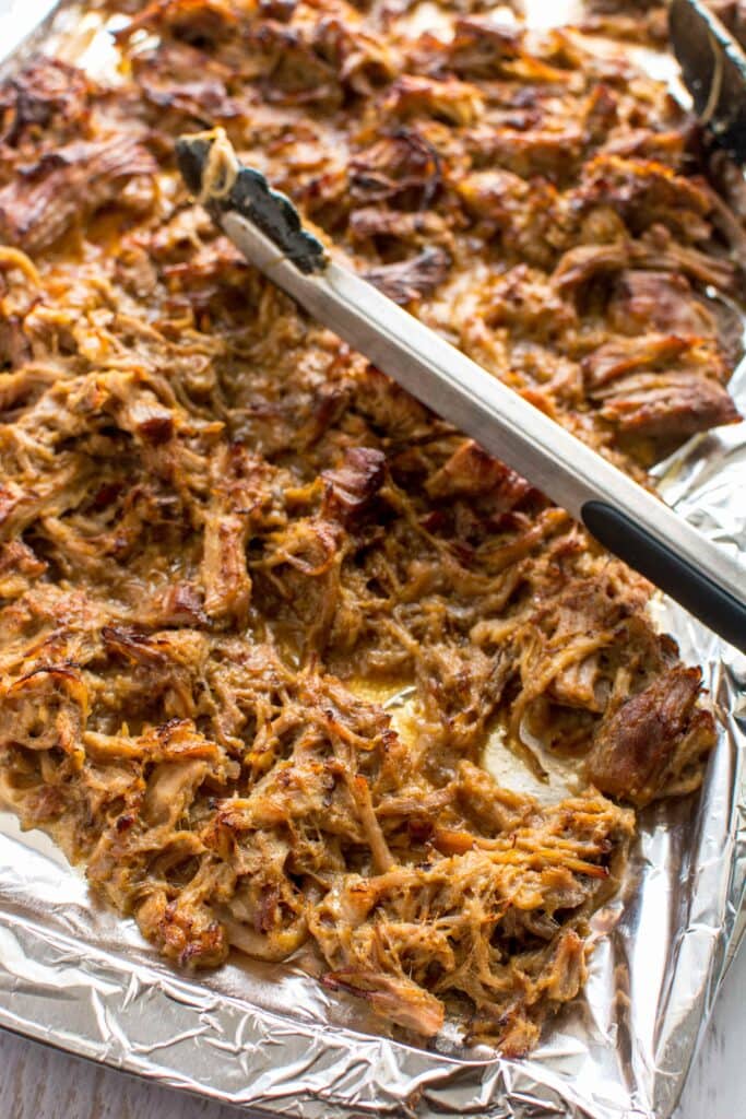 Browned Slow Cooker Honey Mustard Pulled Pork on baking sheet with tongs