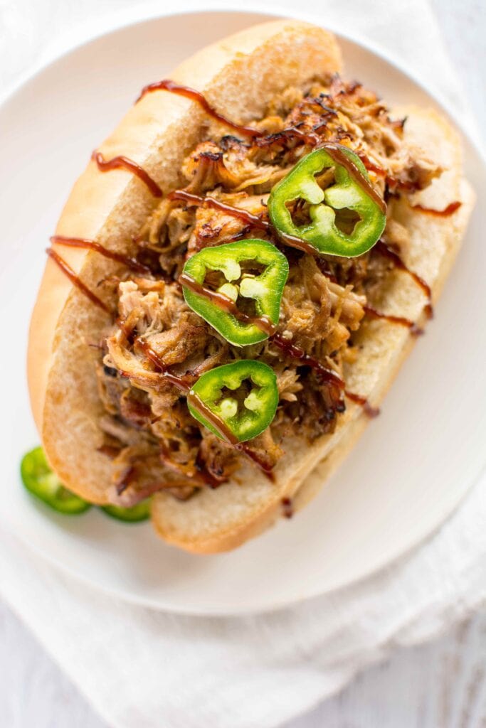 Overhead view of Slow Cooker Honey Mustard Pulled Pork on bun with jalapenos on white plate