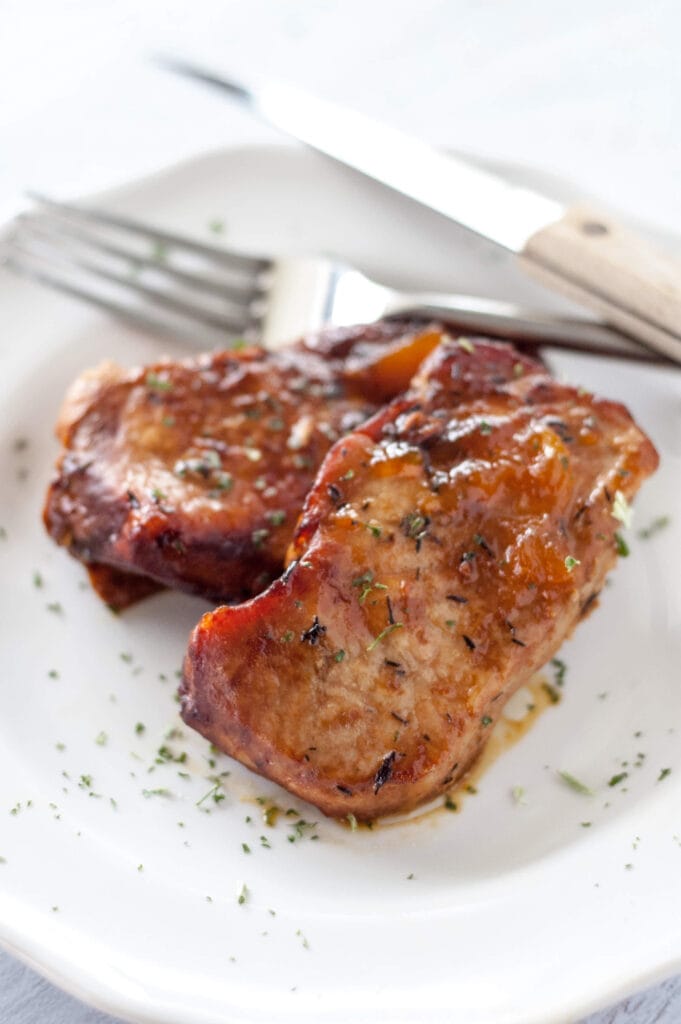 peach glazed pork chops on white plate with knife and fork