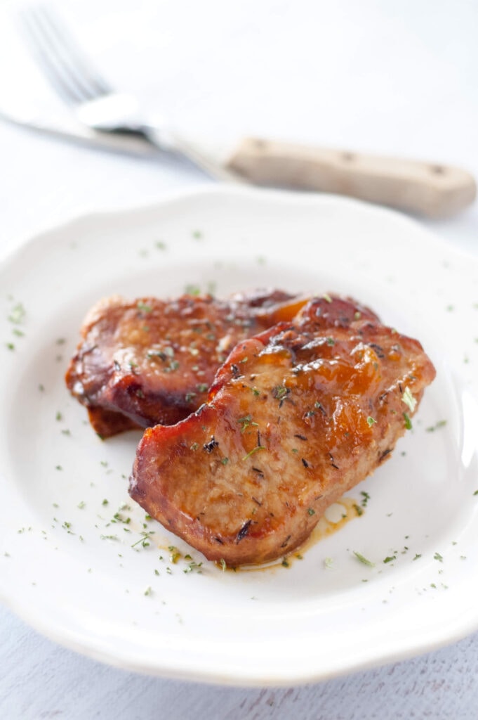 peach glazed pork chops on white plate with knife and fork in background
