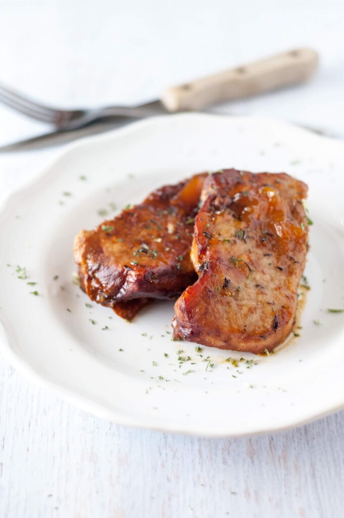 peach glazed pork chops on white plate with fork and knife in background