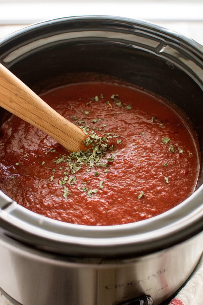 Slow Cooker Roasted Garlic Marinara on wooden spoon and slow cooker