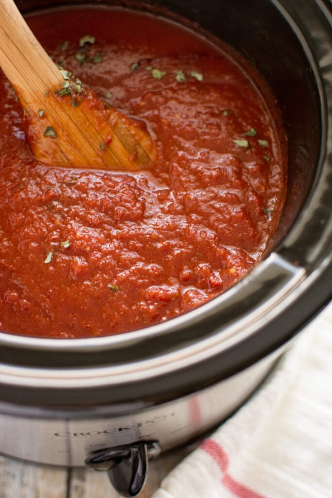 Slow Cooker Roasted Garlic Marinara on wooden spoon and slow cooker