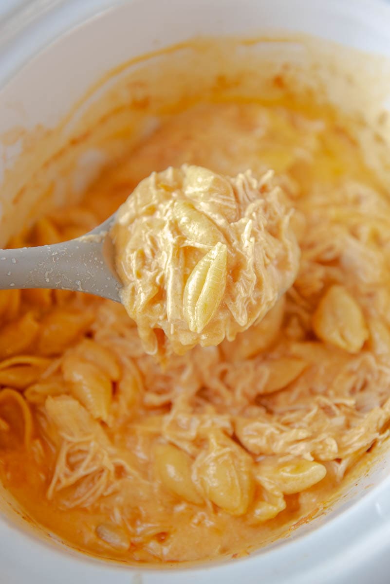 spooning out buffalo chicken Mac and cheese from white slow cooker