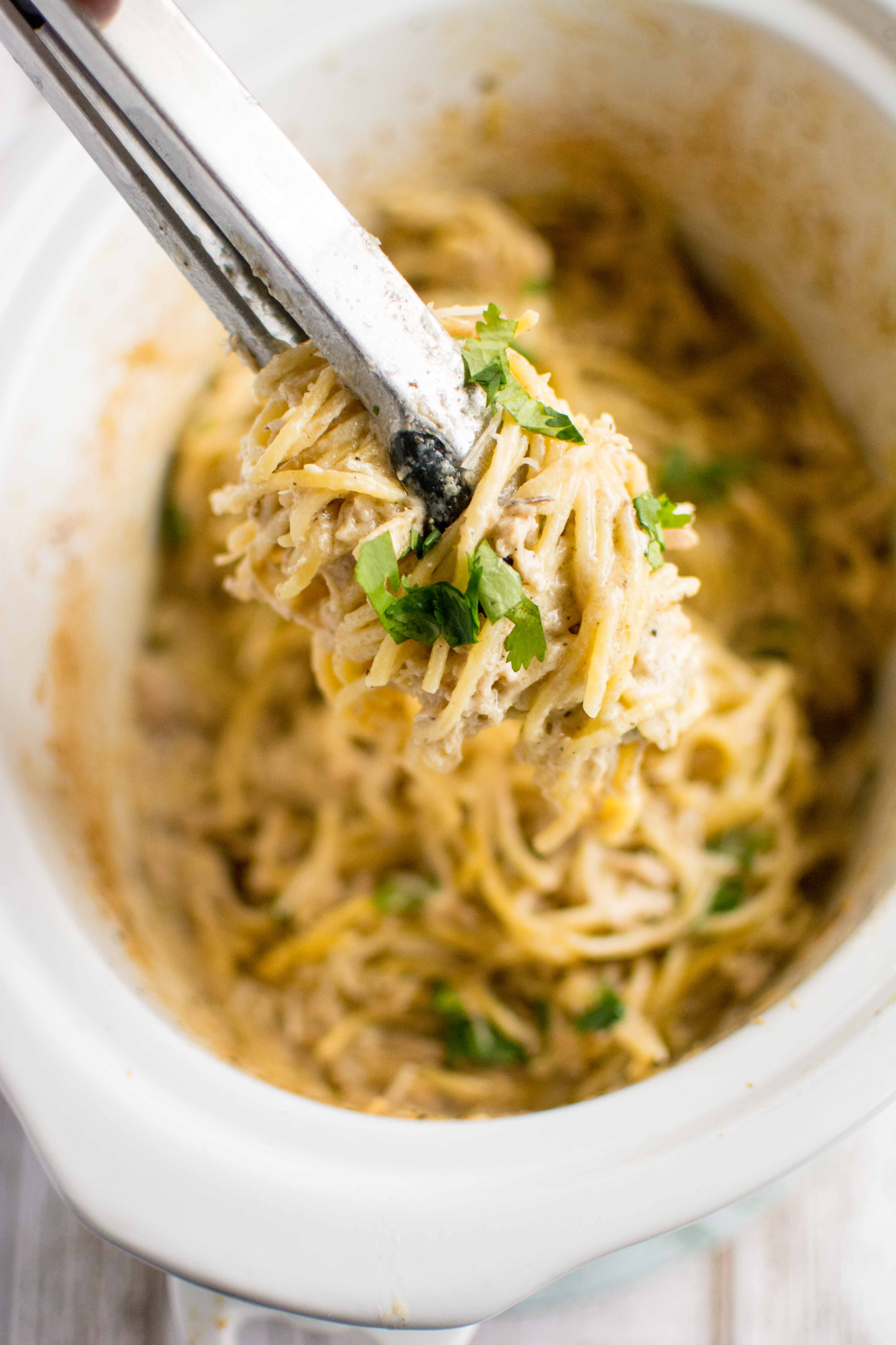 chicken spaghetti in white slow cooker with closeup of tongs with spaghetti 