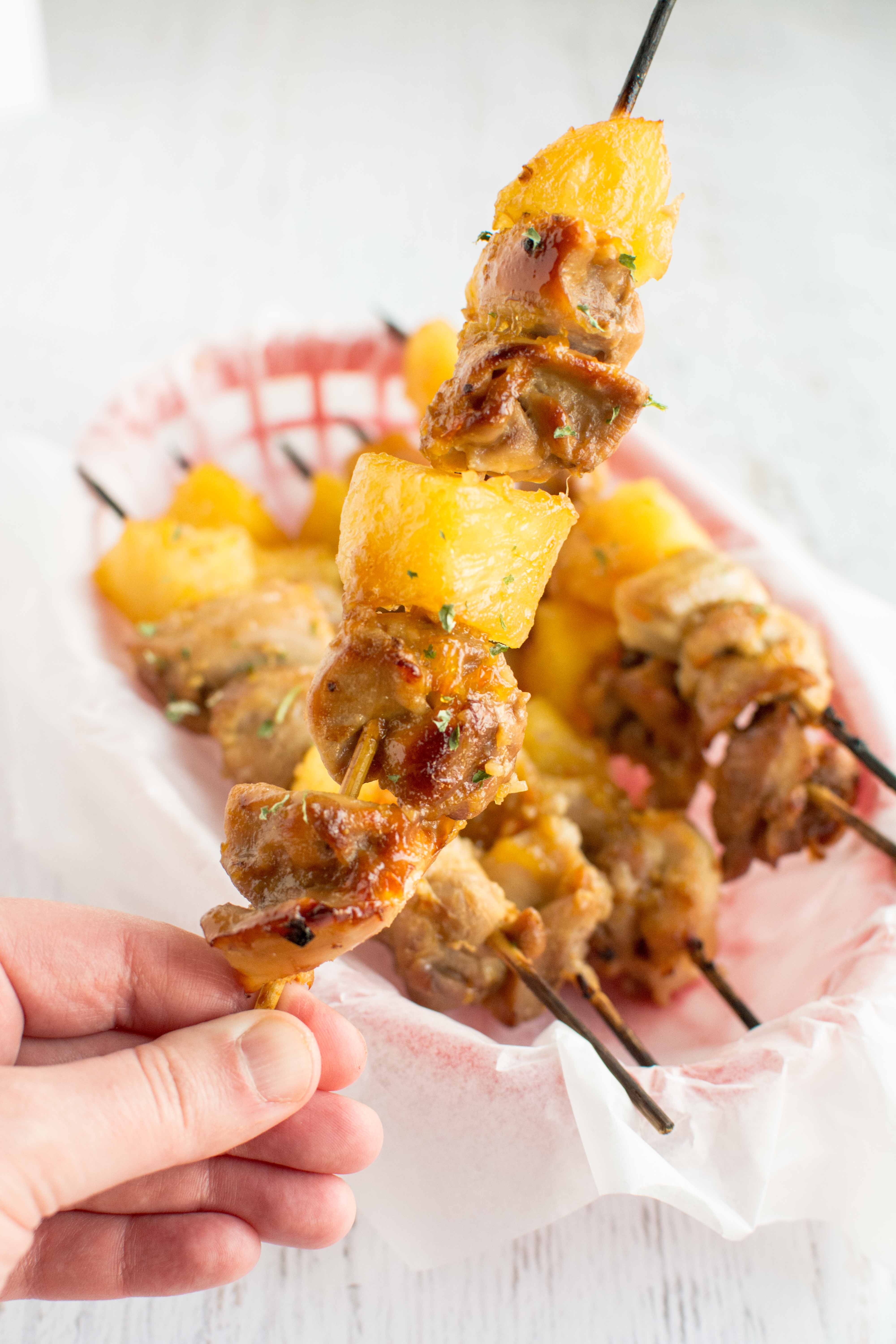 slow cooker chicken skewers in parchment paper lined red basket with one skewer held up