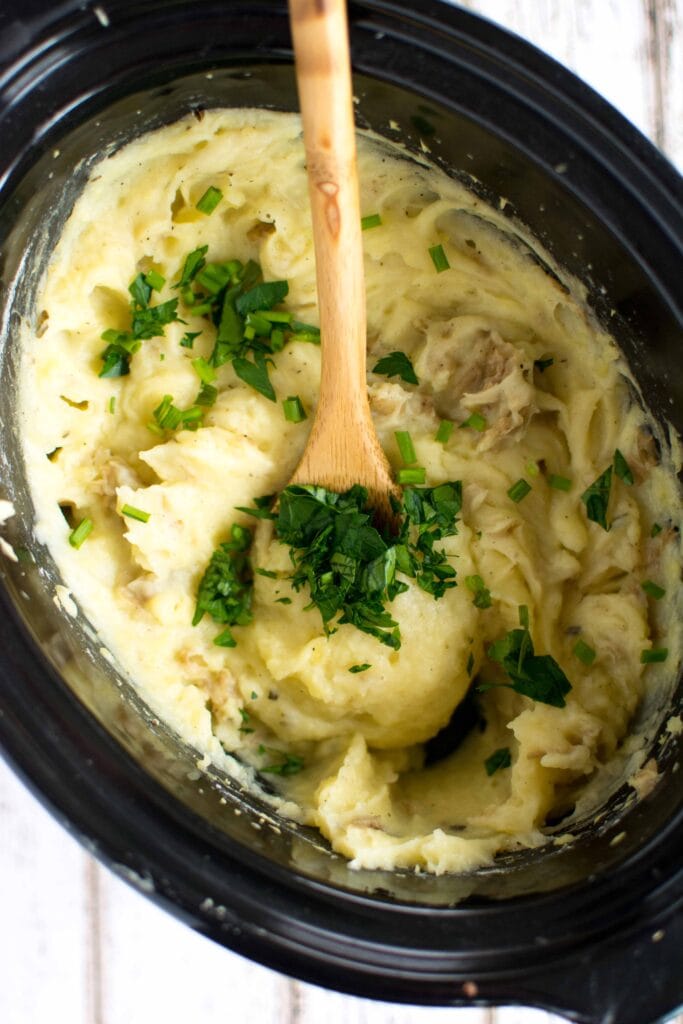 mashed potatoes in slow cooker with wooden spoon