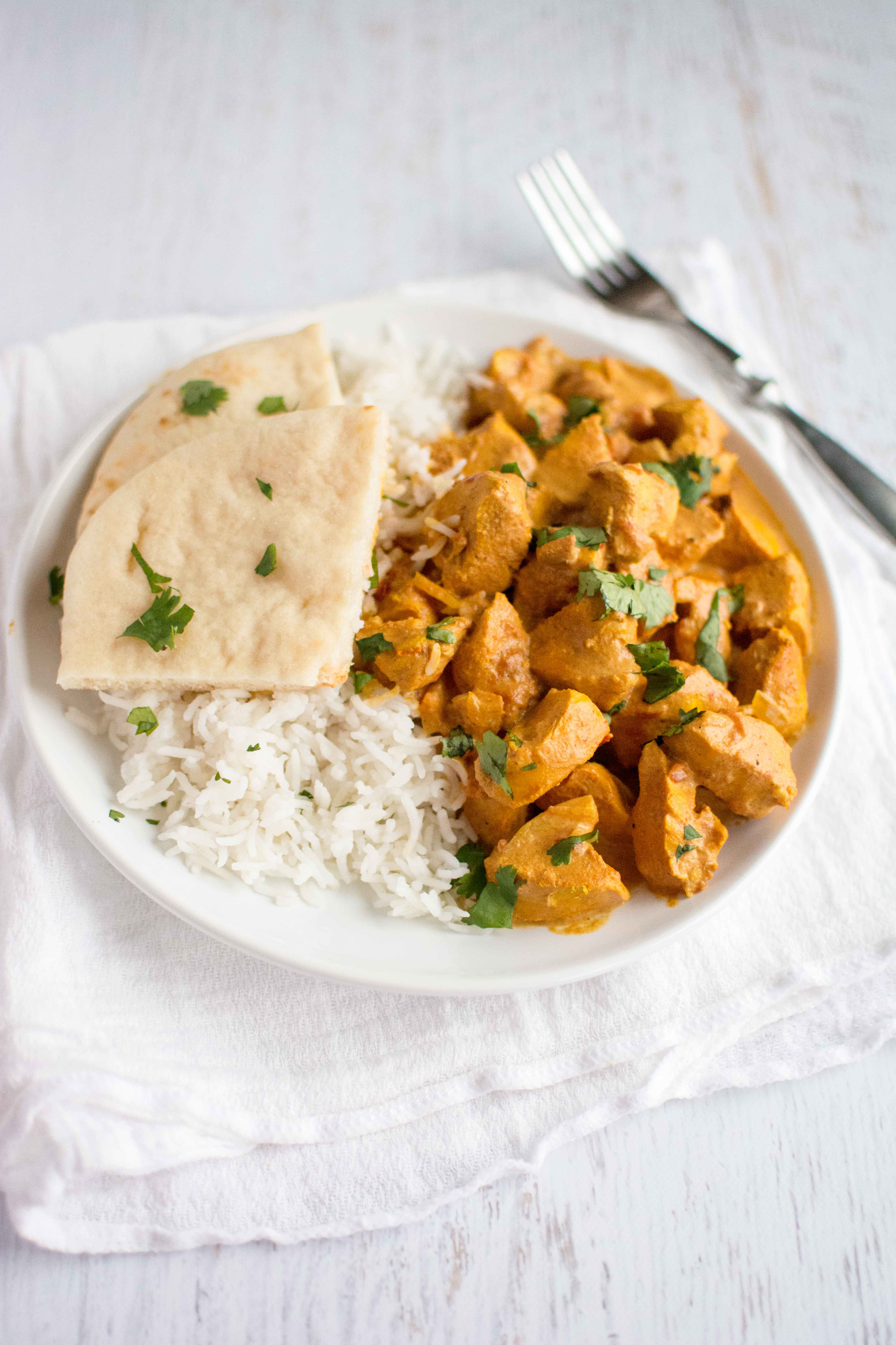 tikka masala, rice and naan in white plate with fork on side