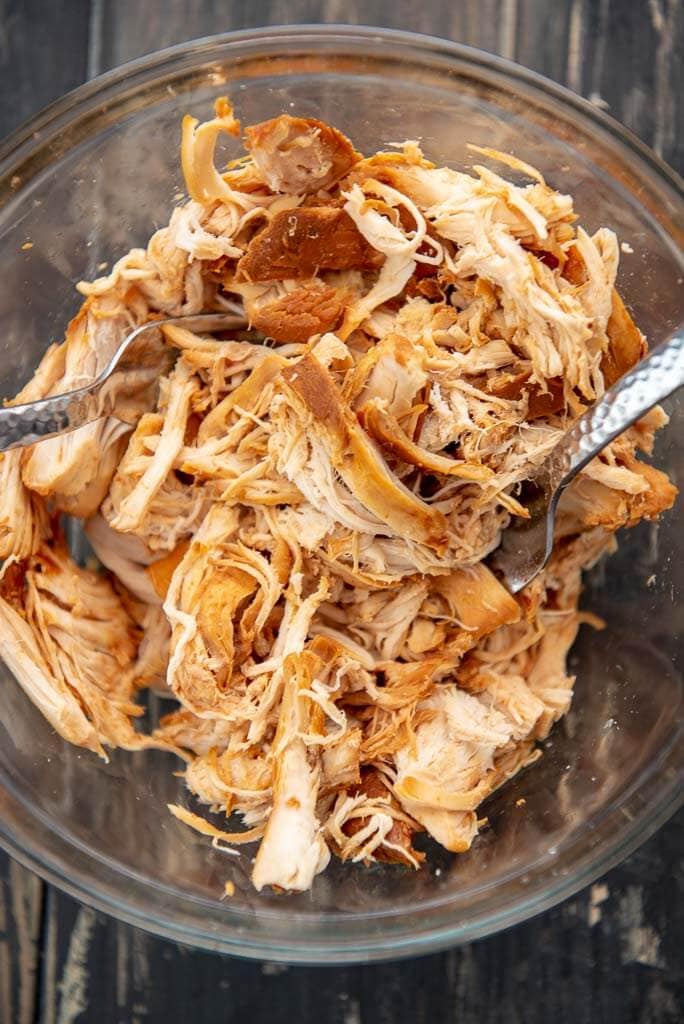 shredded chicken with forks in a glass bowl for pulled chicken