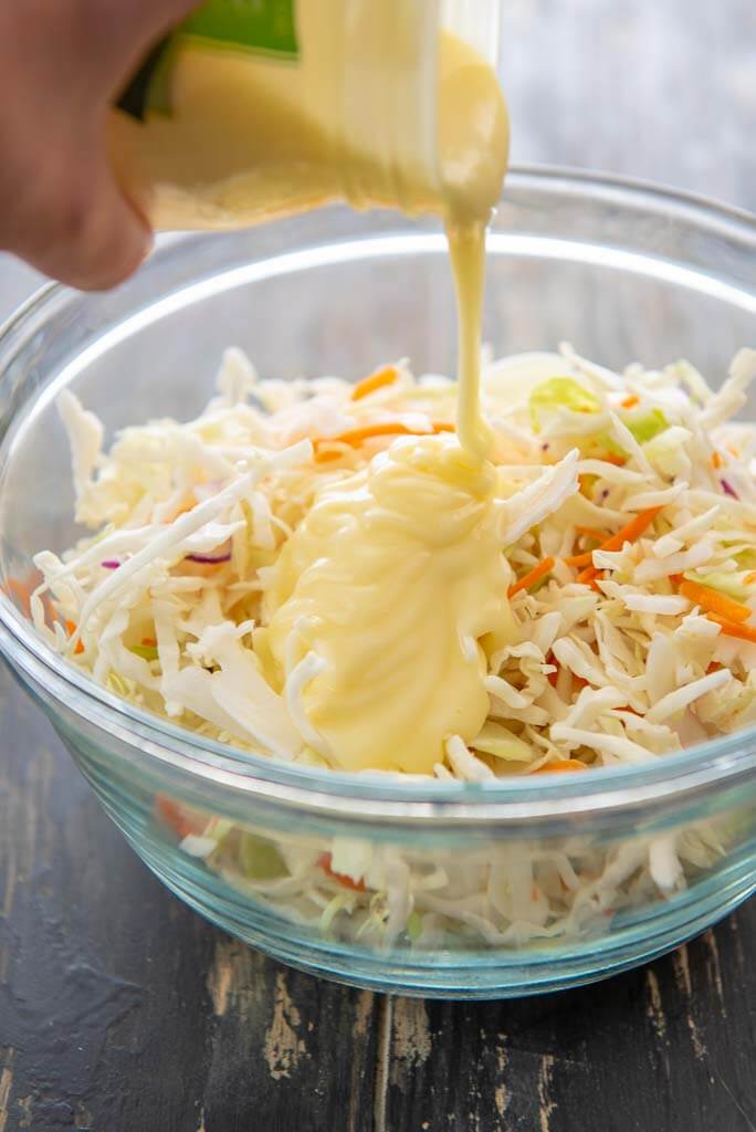 pouring dressing onto coleslaw in a glass bowl